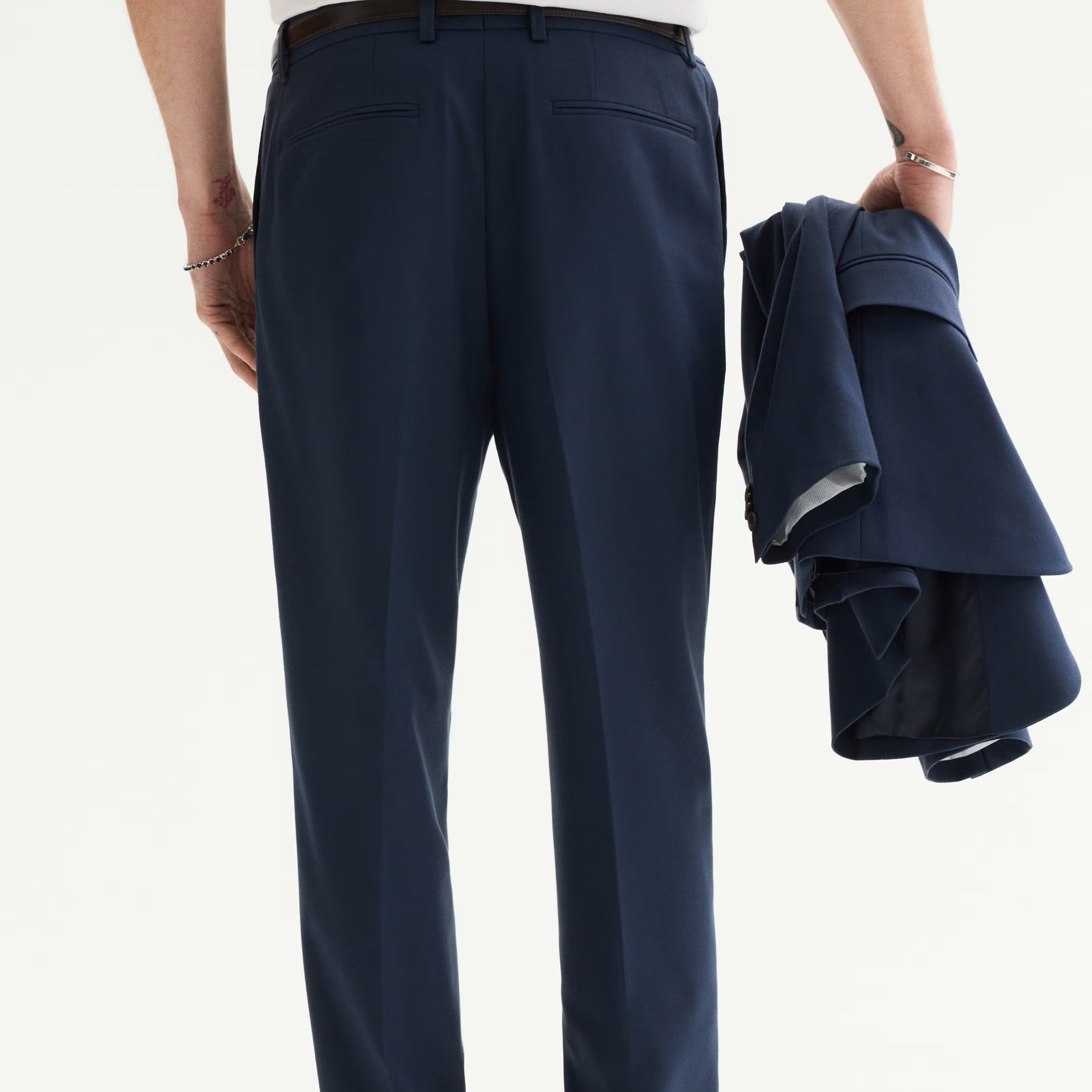 Person wearing navy pants holding a folded navy jacket on a white background