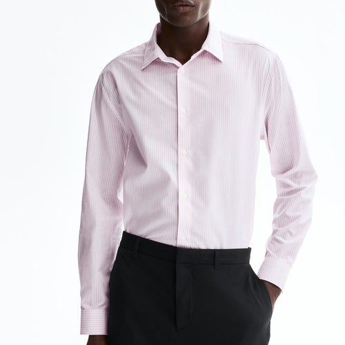 A man wearing a light pink long-sleeve dress shirt with black trousers, photographed against a plain white studio background.