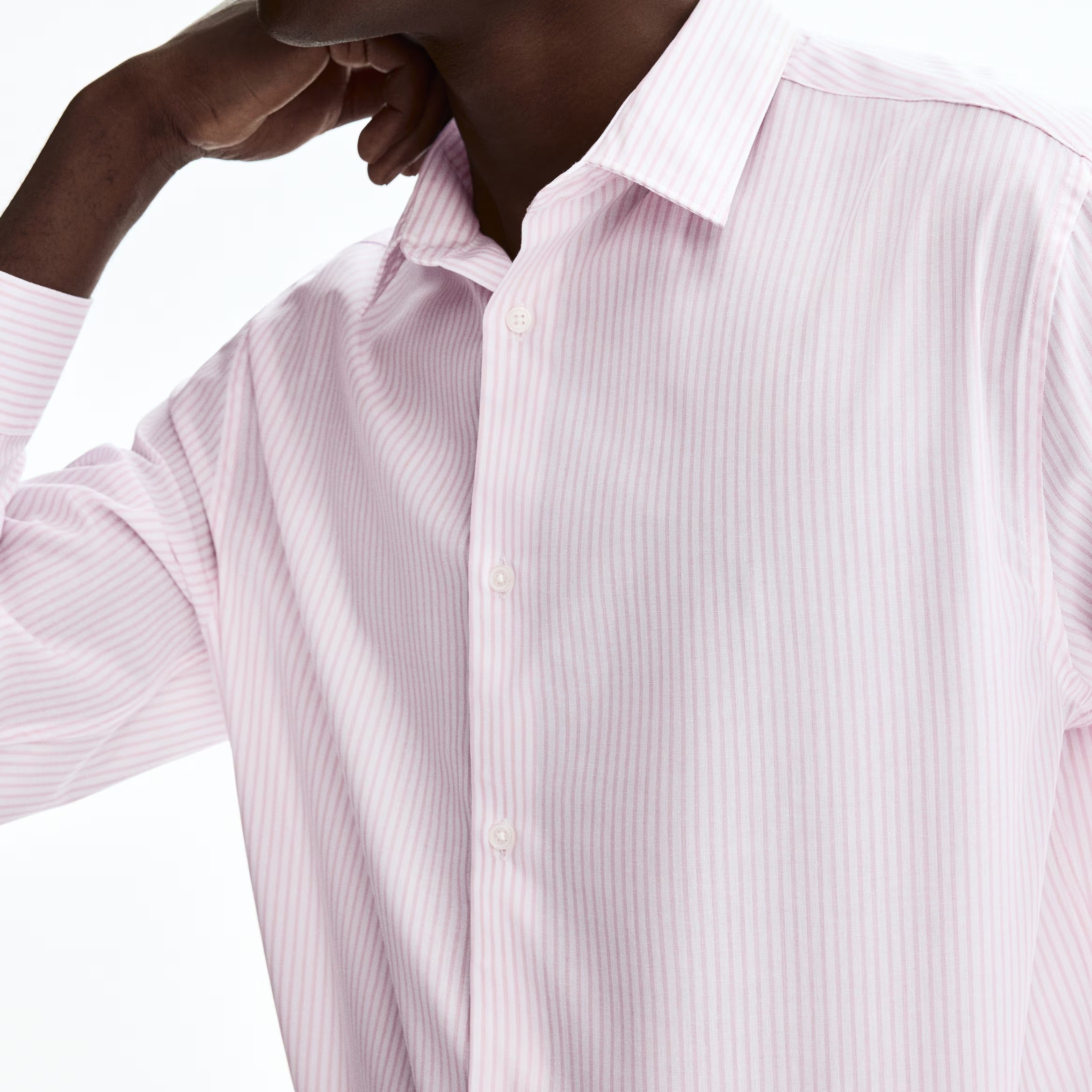 A close-up of a man wearing a light pink and white vertically striped button-down dress shirt, shown from the chest up against a plain white background.