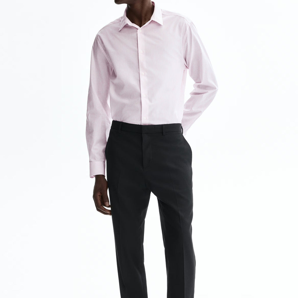 A man modeling a light pink long-sleeve dress shirt and black trousers against a plain white studio background.