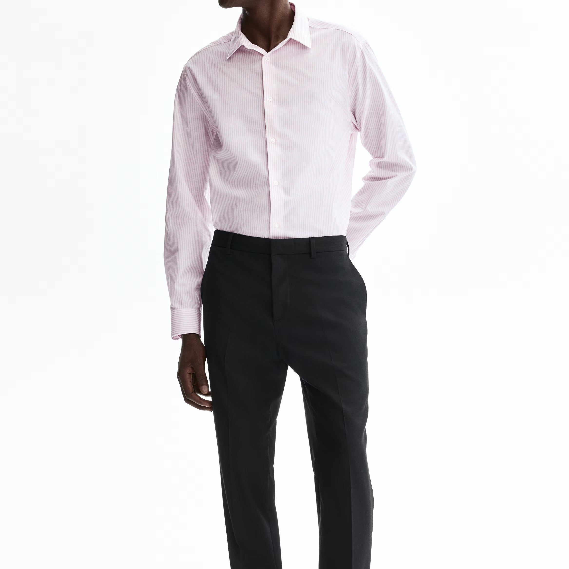 A man modeling a light pink long-sleeve dress shirt and black trousers against a plain white studio background.