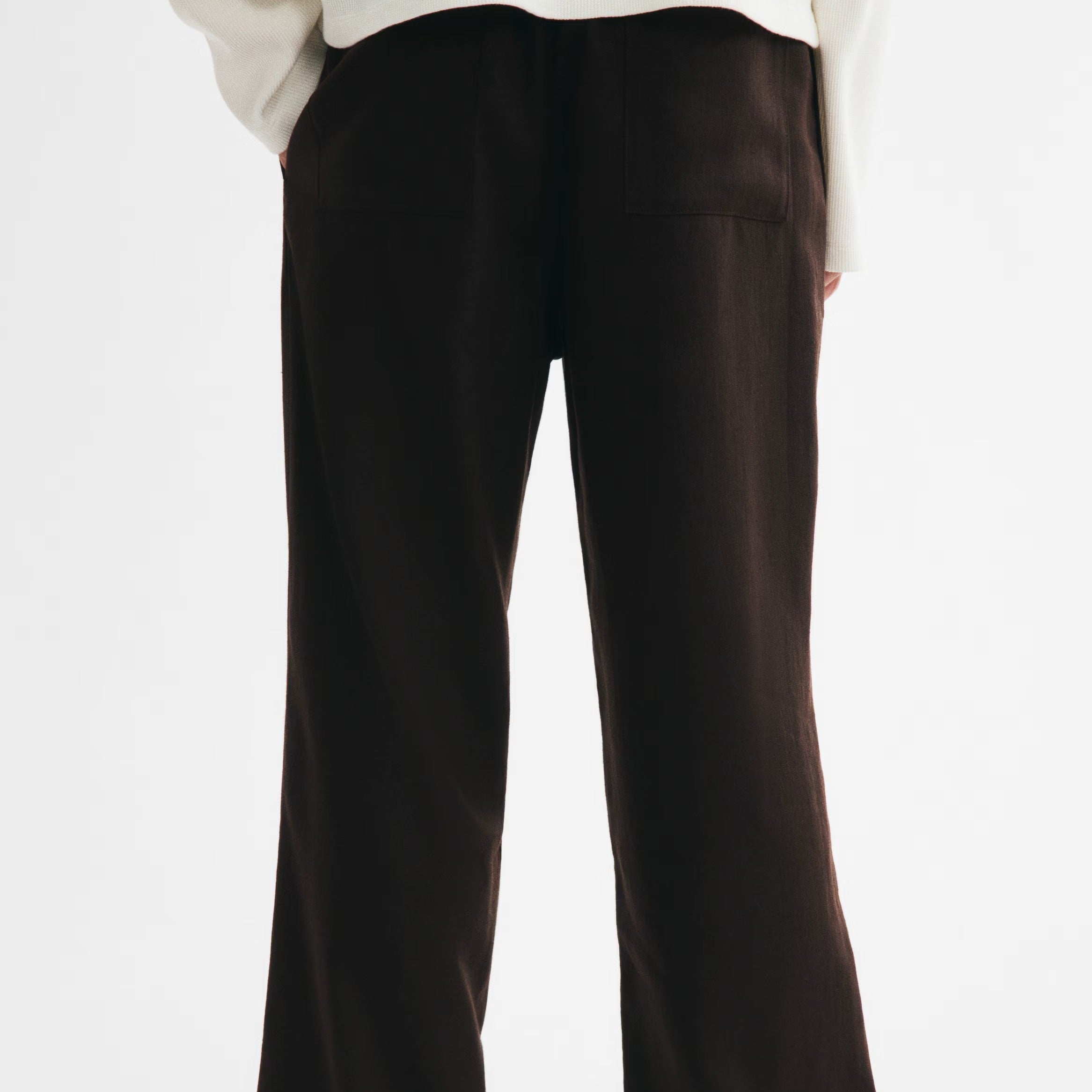 A person shown from the back wearing dark brown wide-leg trousers and a white long-sleeve top against a plain light background.