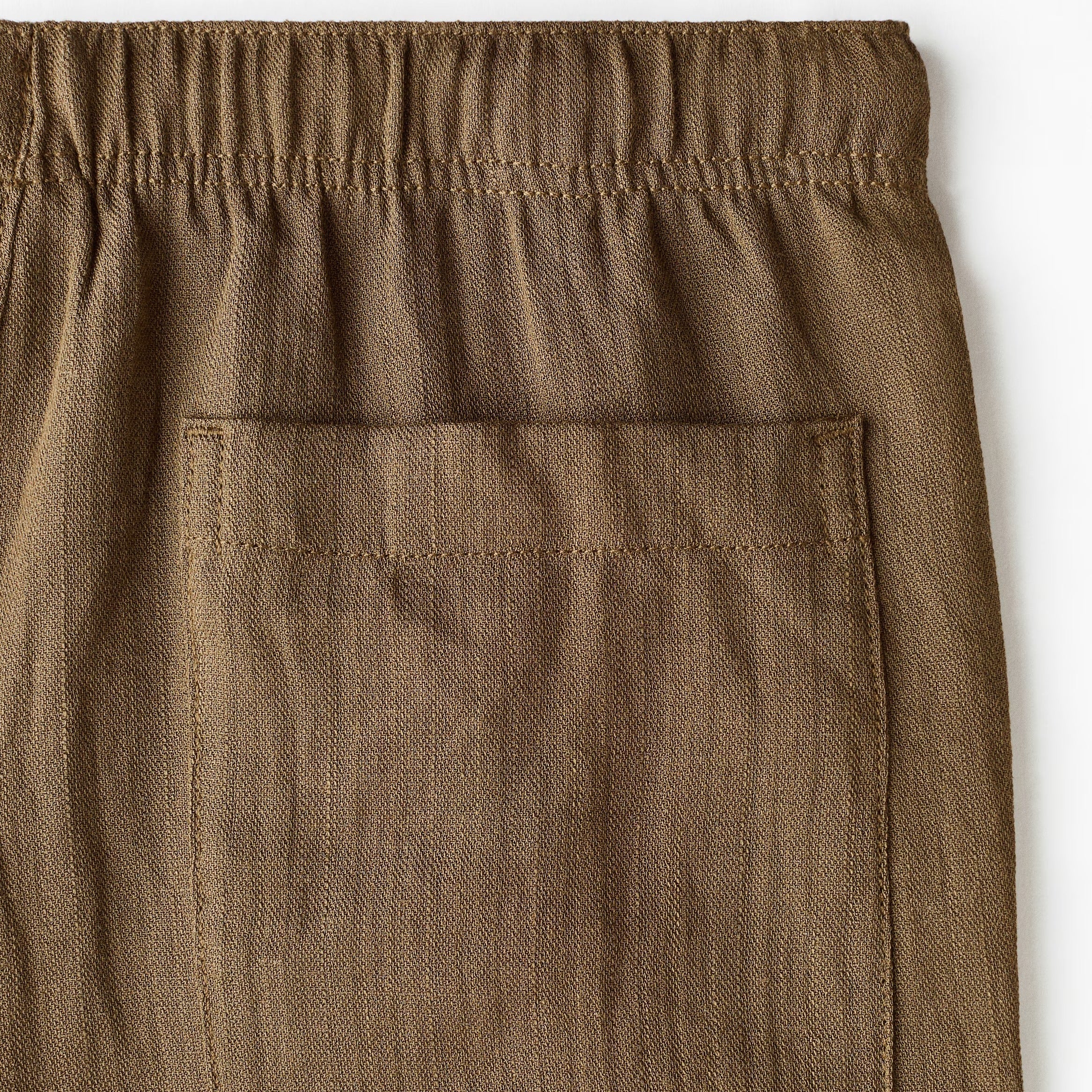 Close-up of brown textured trousers showing an elastic waistband and a front patch pocket.