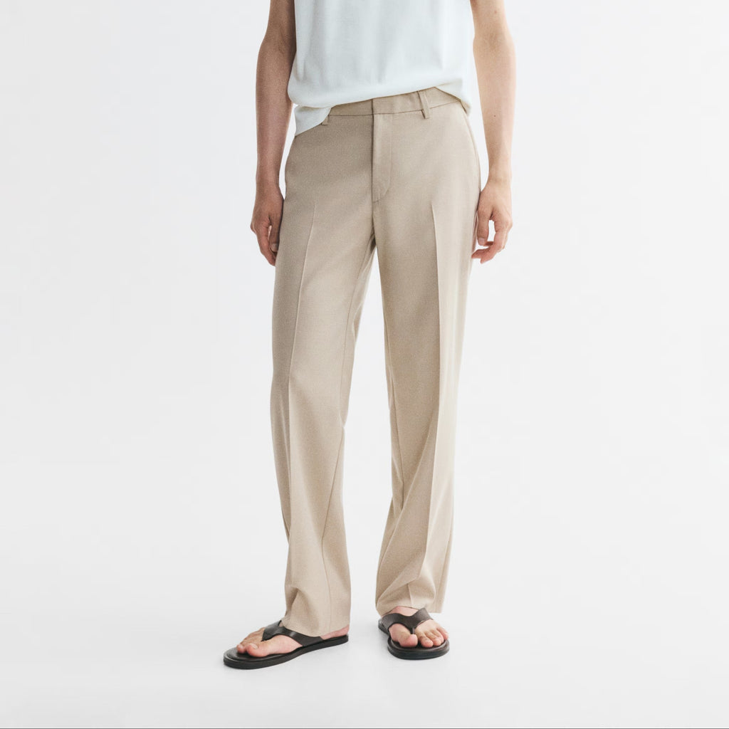 A man modeling a white short-sleeve henley shirt and beige trousers with black sandals, standing against a plain white studio background.