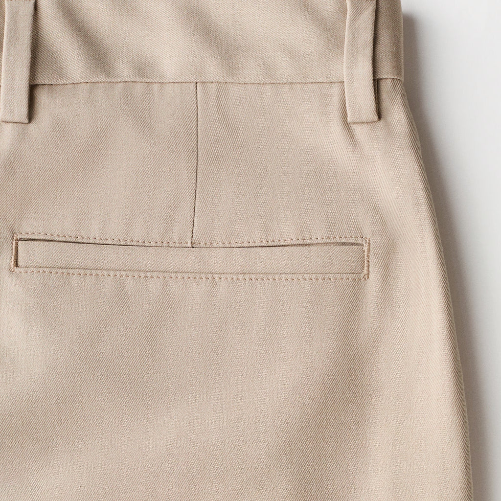 Close-up of the back waistband and rear pocket of light beige trousers, showing clean stitching and fabric texture against a plain light background.